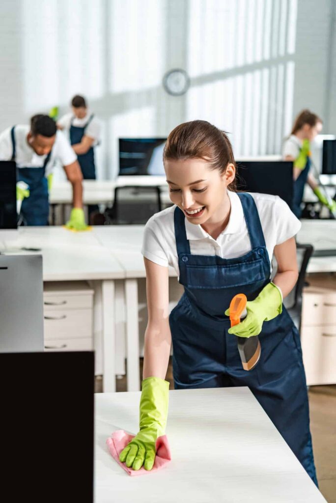 cheerful-cleaner-in-overalls-cleaning-office-desk-with-rag-1.jpg